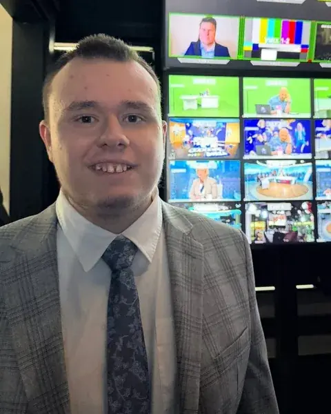 Marcin Jabłoński na tle ściany monitorów reżyserki telewizyjnej